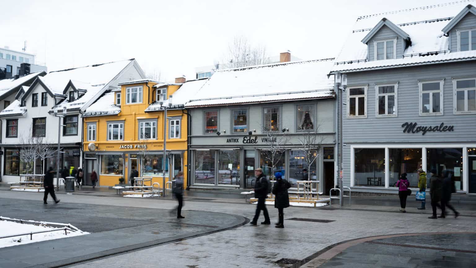 Arctic Frontiers - People walk past colourful snow-covered shops on a street in a European town, braving the chilly embrace of Arctic Frontiers on a crisp winter day.