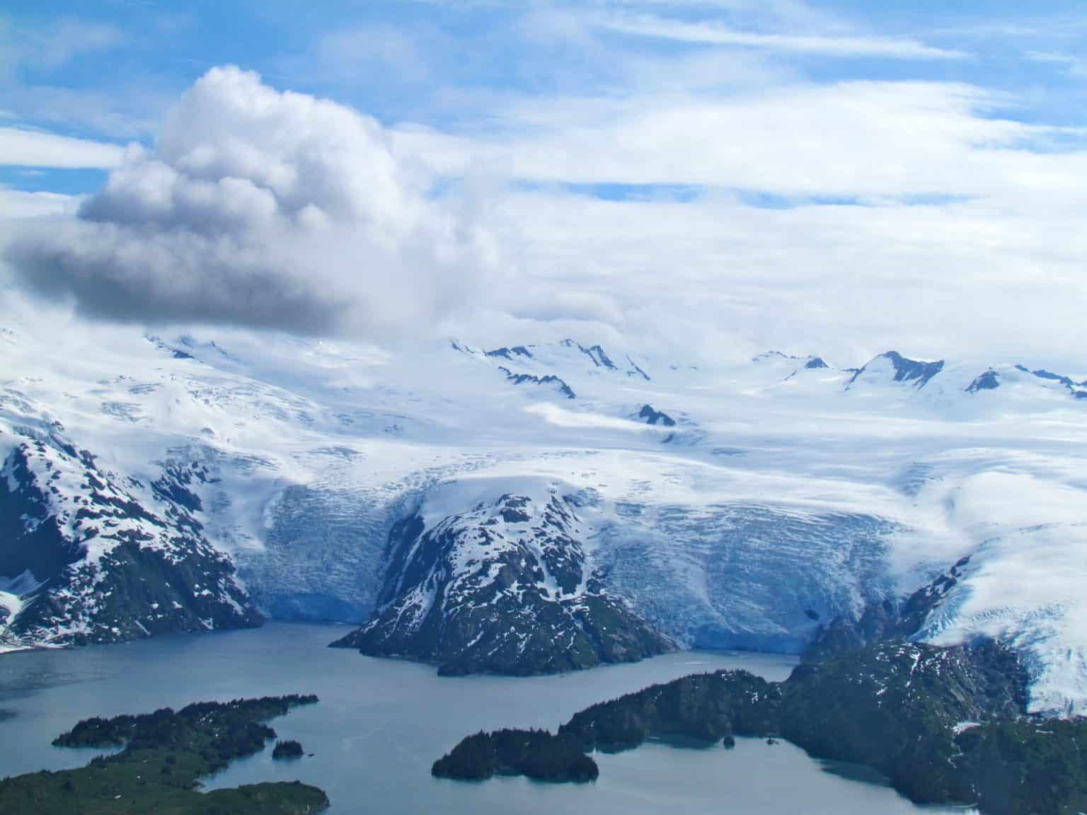 Arctic Frontiers - Snow-covered mountains and a glacier flowing into a bay under a partly cloudy sky capture the dramatic beauty of the Arctic Frontiers.