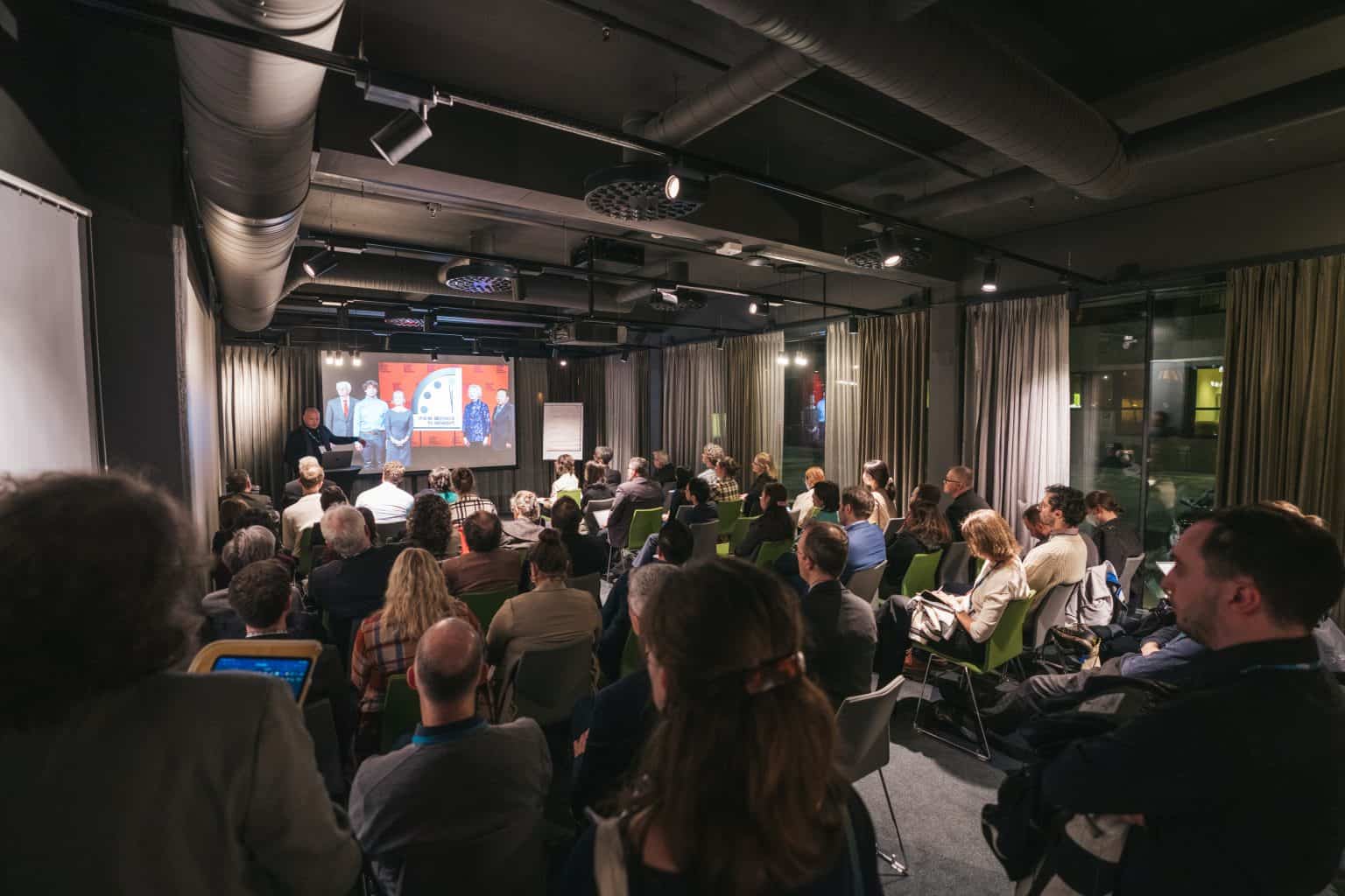 A photo from the back of a packed room of scientists and policy makers listening to someone making a presentation about science diplomacy.