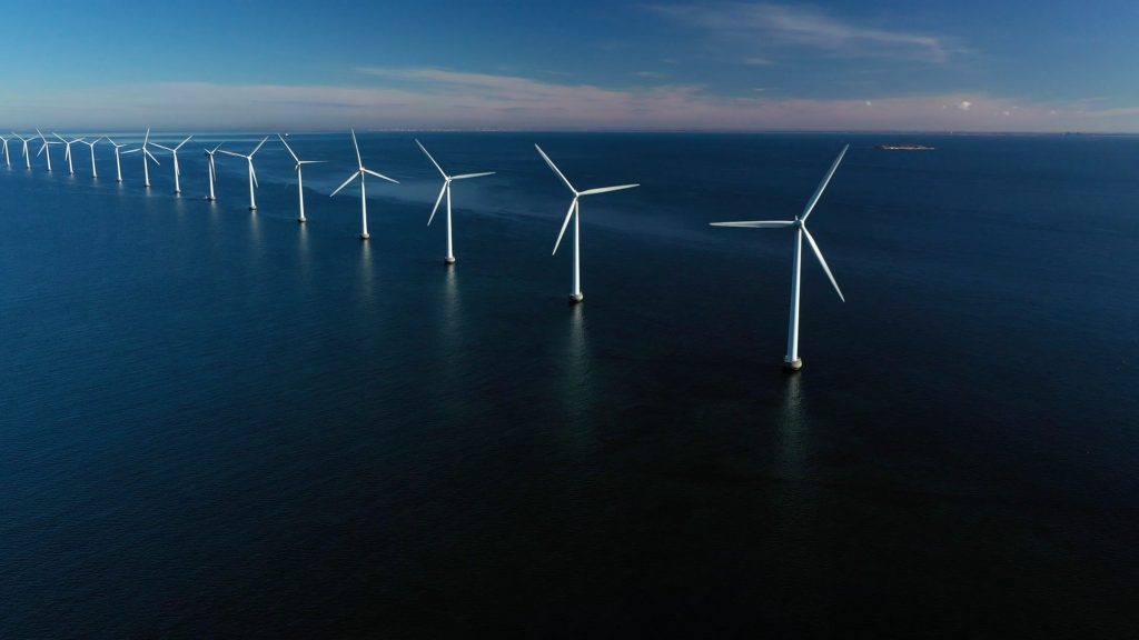 Arctic Frontiers - Aerial view of offshore wind turbines lined up in the sea under a blue sky, captured by Arctic Frontier Partner pictures.