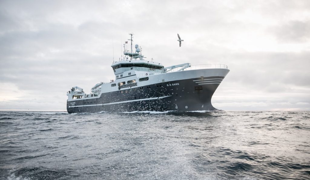 Arctic Frontiers - Large research vessel sailing on the open ocean, featured in Arctic Frontier Partner pictures, with a bird flying overhead under a cloudy sky.