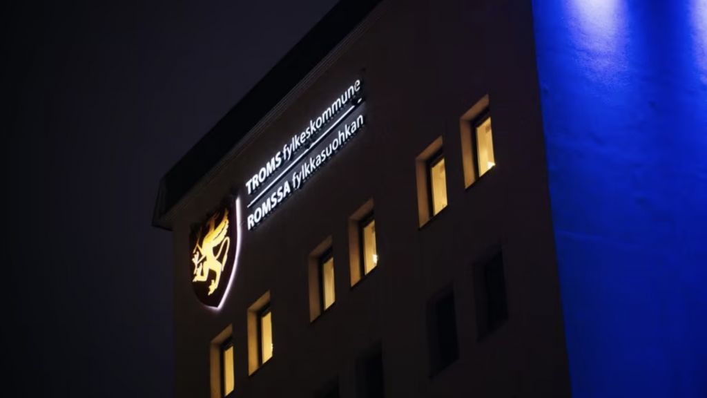 Arctic Frontiers - A building façade at night with lit windows and a sign reading “TROMSØ kommune, ROMSSA Suohkan,” captured in striking Arctic Frontier Partner pictures.