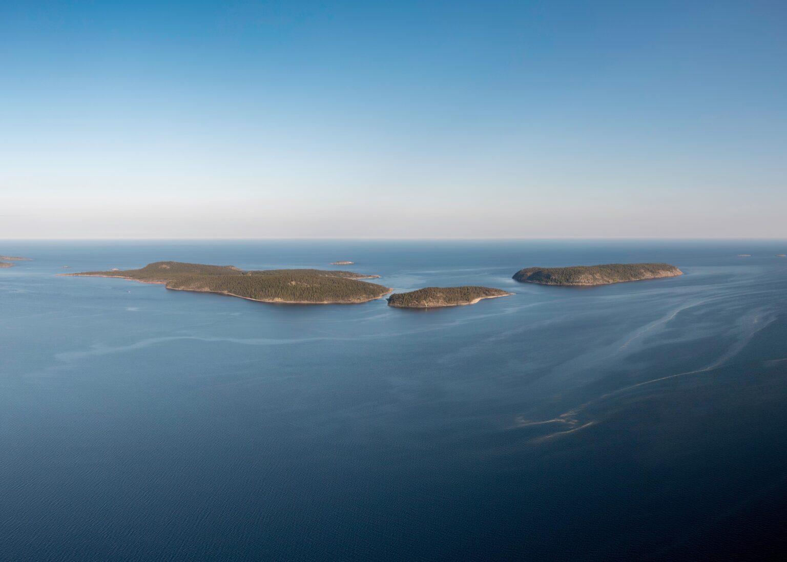 Arctic Frontiers - Aerial view of several green islands surrounded by calm blue water under a clear sky, capturing the serene beauty often explored at Arctic Frontiers.