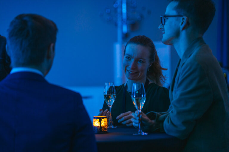 Arctic Frontiers - Three people in formal attire chat and smile around a table with drinks and a candle in blue lighting at Arctic Frontiers – Emerging Leaders 2026.