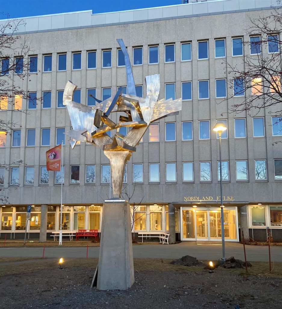 Arctic Frontiers - Abstract metal sculpture on a plinth in front of a modern office building at dusk, featured in Arctic Frontier Partner pictures.