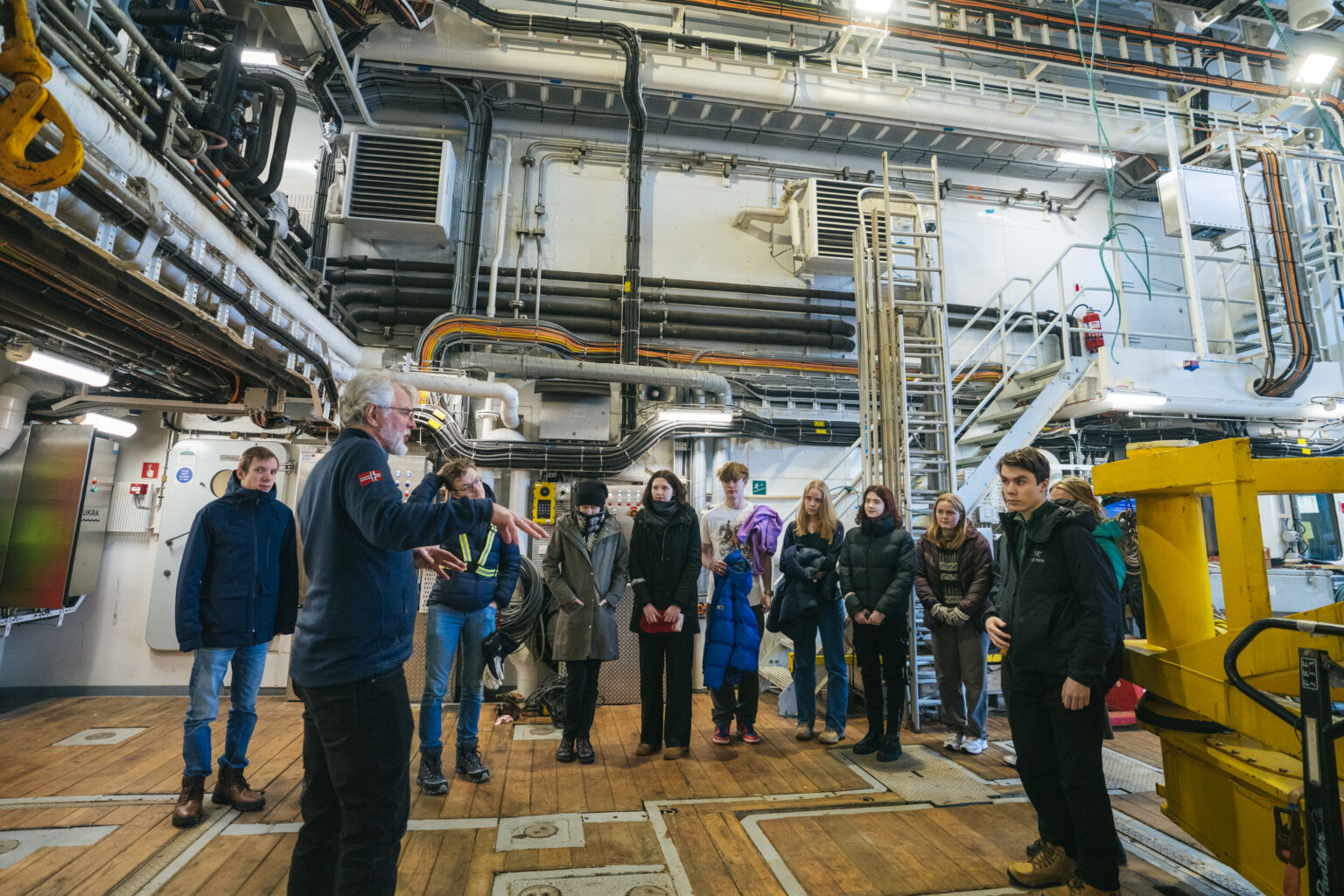 Arctic Frontiers - A group of people listens to a guide inside an industrial facility with pipes and machinery during the Arctic Frontiers - Young Science for Schools programme.