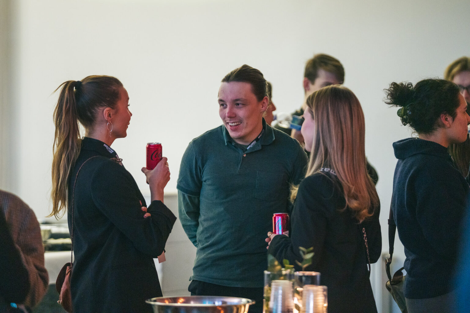 Arctic Frontiers - Three people talk and hold fizzy drink cans at a social gathering during the Arctic Frontiers - 2025 conference Student Forum; others are visible in the background.