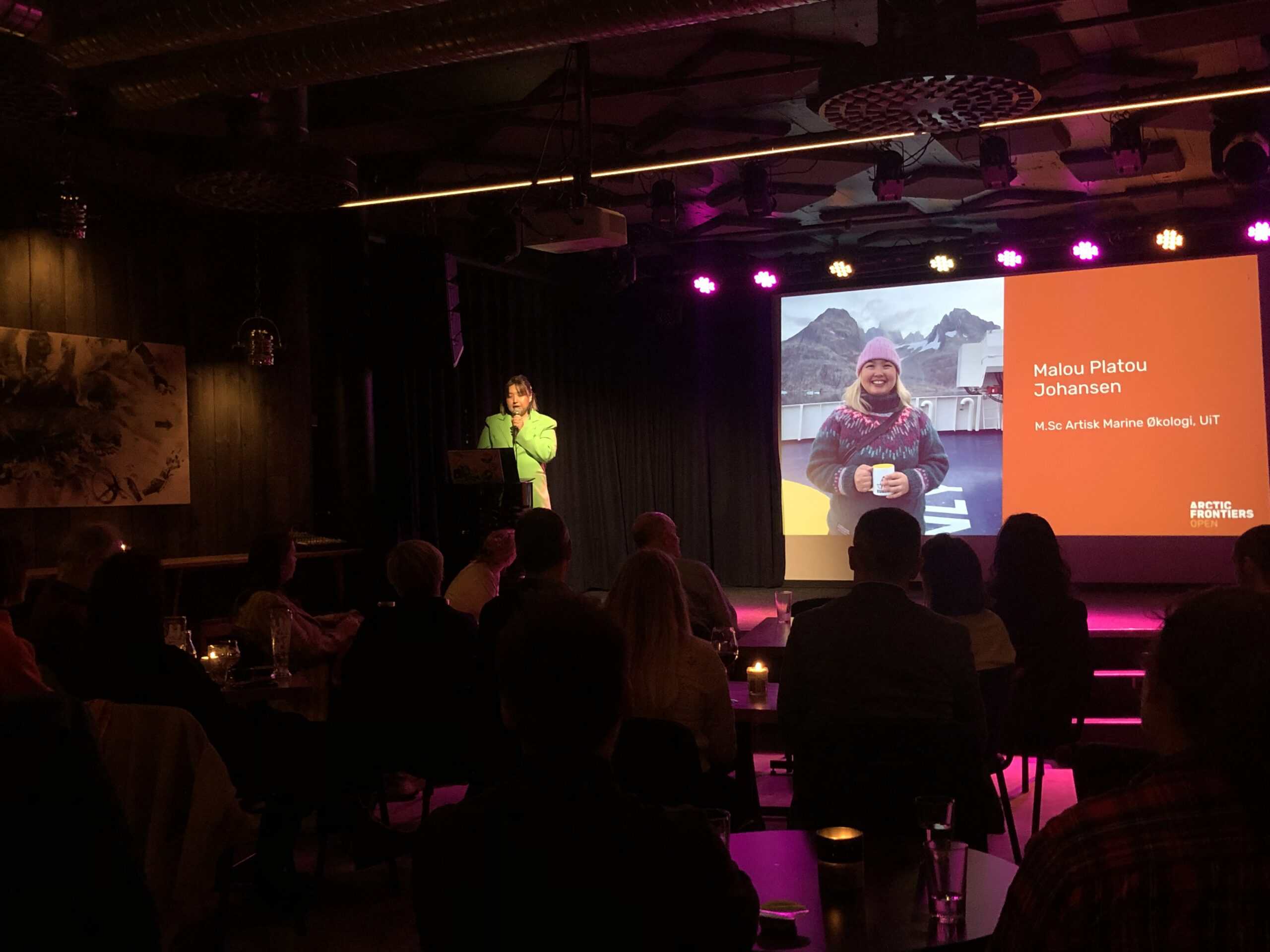Arctic Frontiers - A speaker presents on stage at Arctic Frontiers - Geoengineering open; a slide shows a woman smiling outdoors and her name, Malou Platou Johansen.