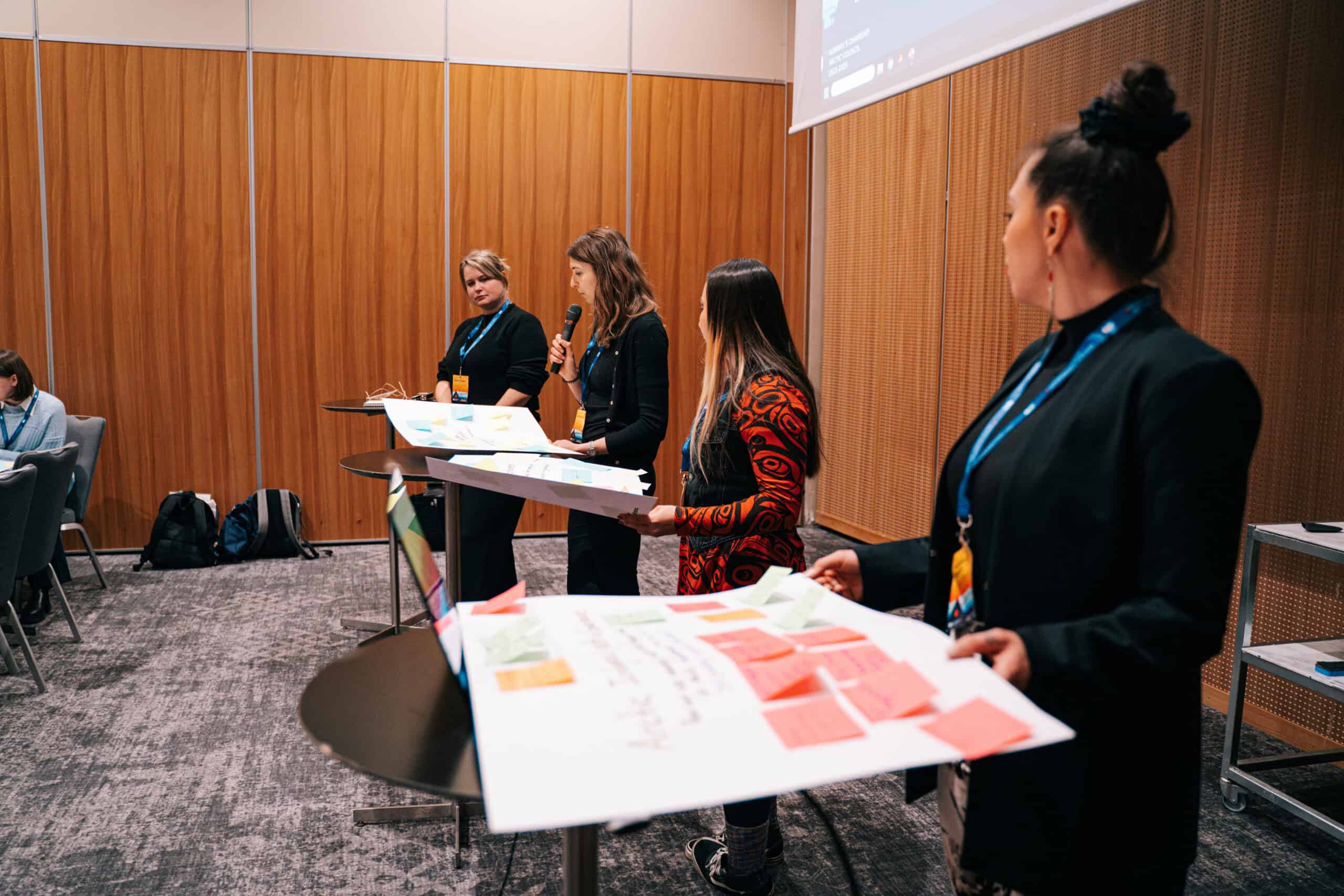 Arctic Frontiers - Four women stand at lecterns, discussing and holding boards with colourful sticky notes in a conference room at the Arctic Frontiers - Emerging Leaders Alumni Network event.