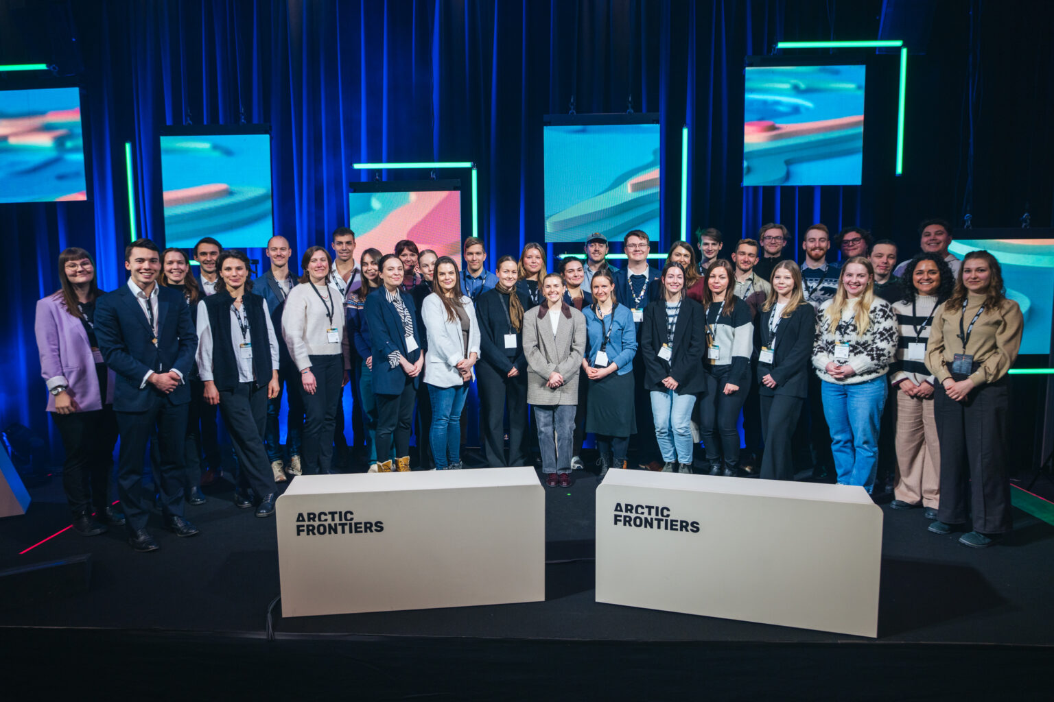 Arctic Frontiers - A group of people pose together on stage at the Arctic Frontiers 2025 conference Student Forum, with screens and lights illuminating the background.