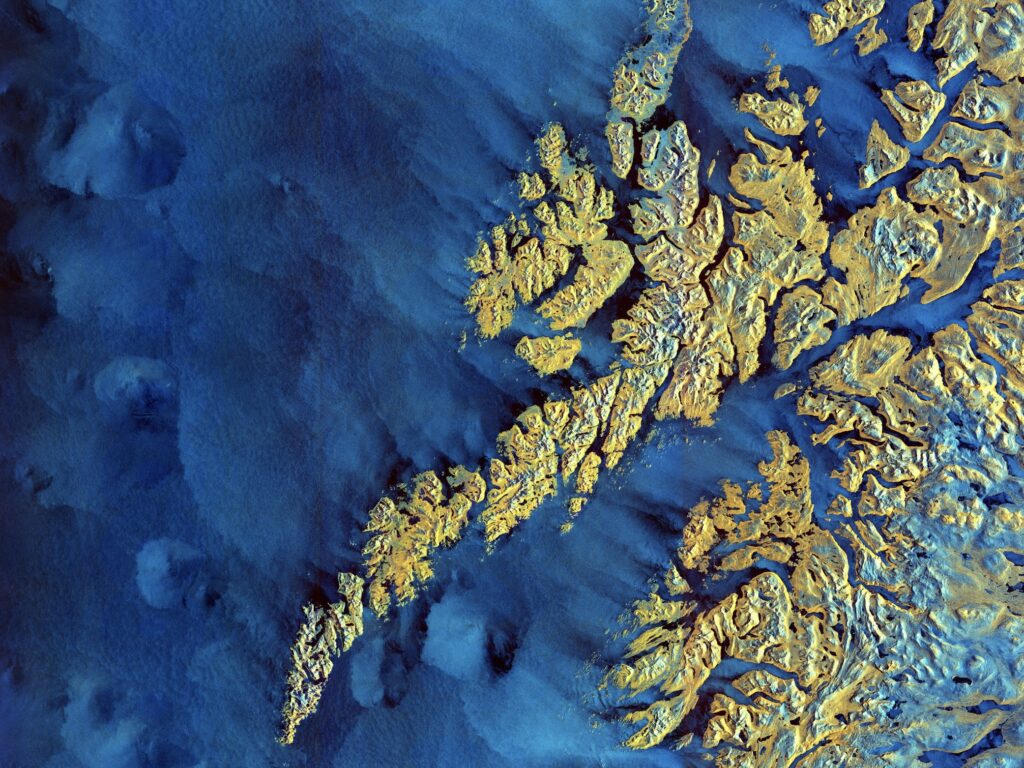 Arctic Frontiers - Aerial view of rugged, yellow and orange landforms surrounded by deep blue water, captured by Arctic Frontier Partner pictures.