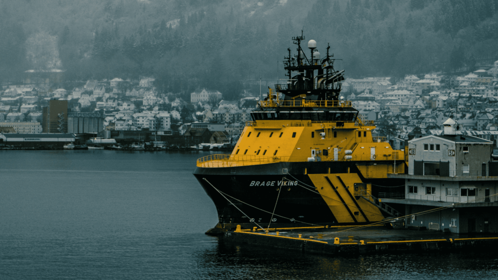 Arctic Frontiers - A large yellow and black ship docked near a misty town by the harbour, with hills in the background, stands ready to face challenges and hybrid threats.