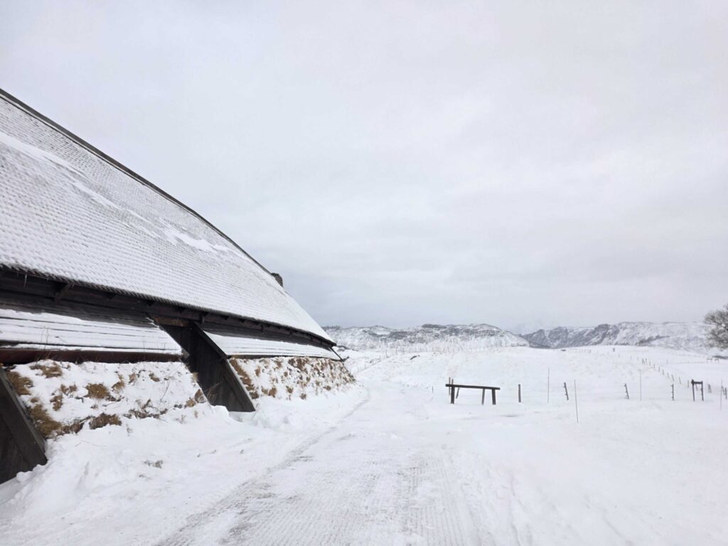 Arctic Frontiers - A snow-covered road passes a building with a sloping roof amid a snowy, mountainous landscape.