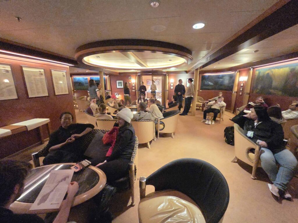 Arctic Frontiers - People sit and talk in a cosy lounge with warm lighting and comfortable chairs, some reading or relaxing.