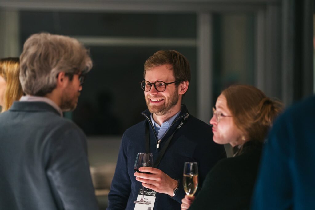 Arctic Frontiers - Three people chat and hold drinks at an indoor event, smiling and wearing conference name badges.