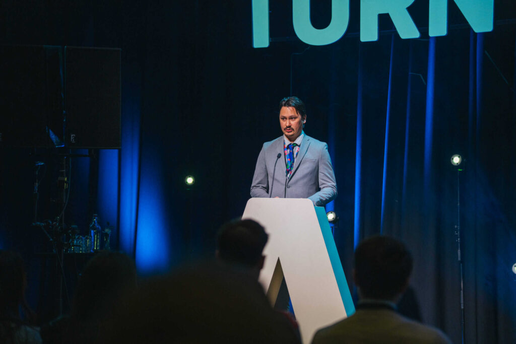 Arctic Frontiers - Man in a suit speaks at a lectern on a blue-lit stage, audience visible in the foreground.