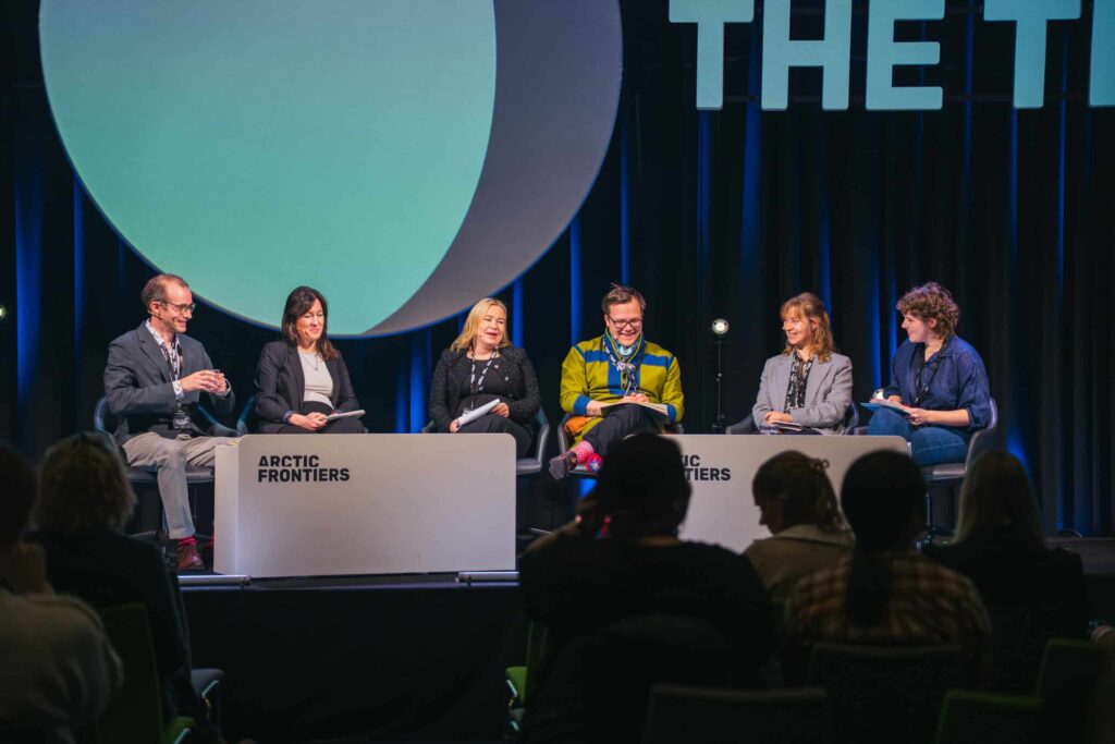 Arctic Frontiers - Six people sit on stage in a panel discussion at Arctic Frontiers, facing an audience under stage lights.