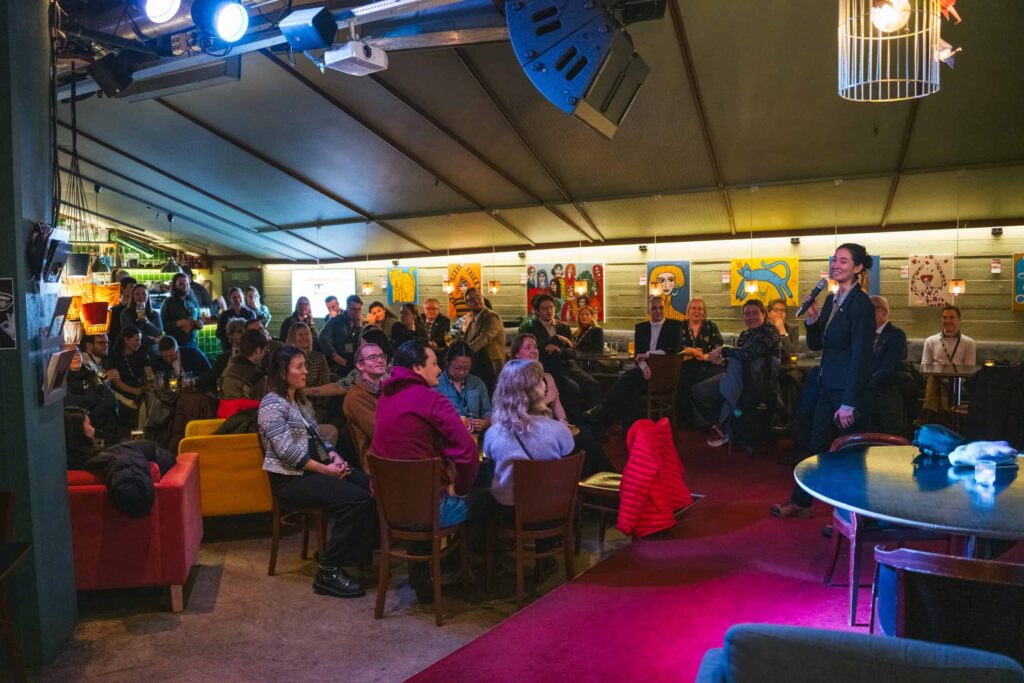 Arctic Frontiers - A person speaks to an attentive audience in a cosy, dimly-lit venue with colourful artwork on the walls.