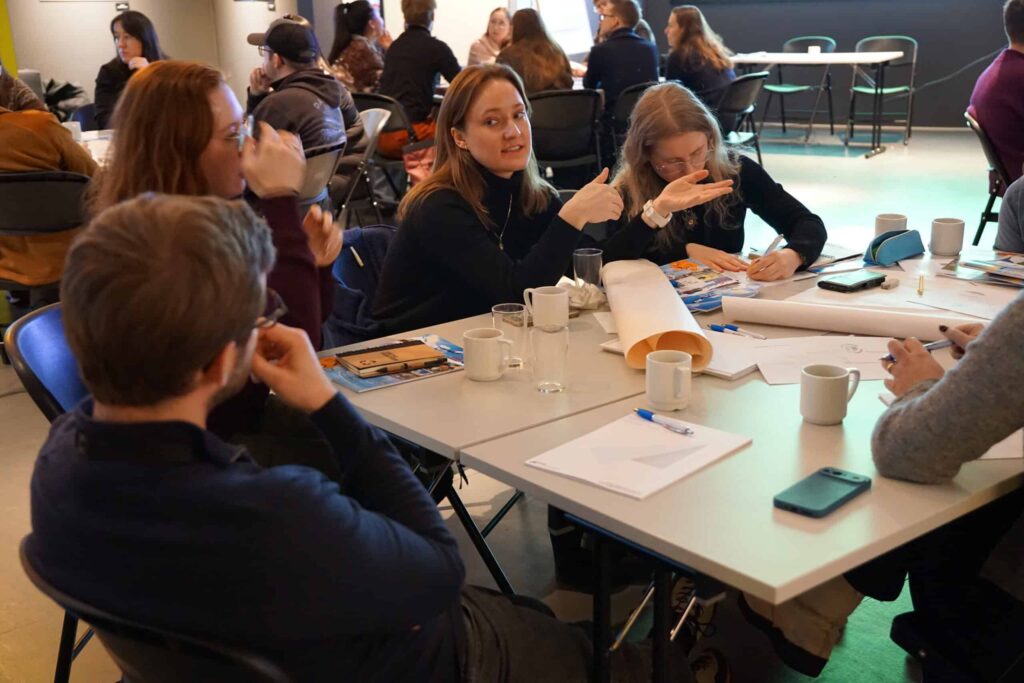 Arctic Frontiers - People sit around tables talking, writing, and working with papers and coffee in a collaborative meeting.