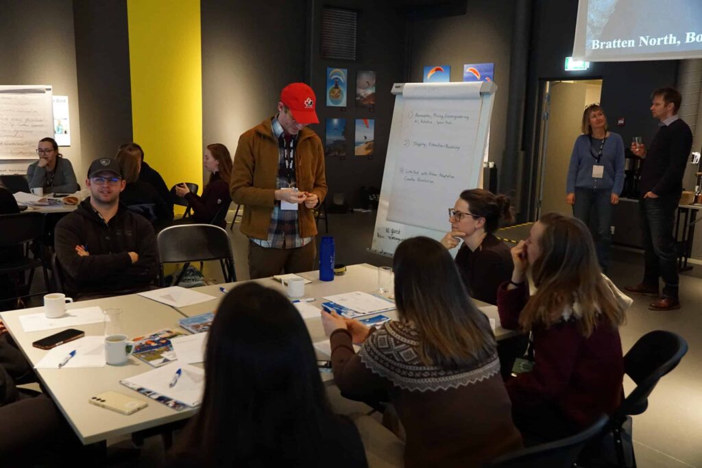 Arctic Frontiers - People sit and talk round tables in a meeting room, with a flipchart and presentation in the background.