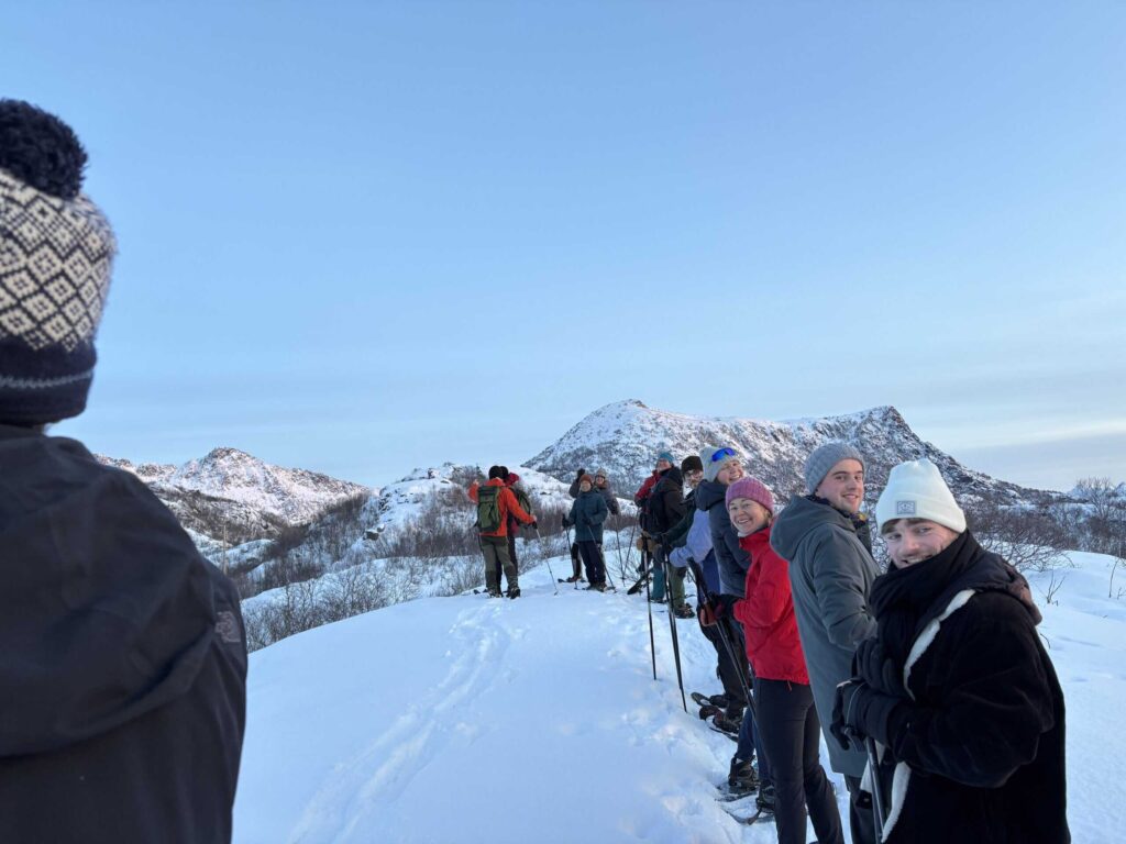 Arctic Frontiers - A group of people in winter clothing stand on a snowy hill with mountains in the background.